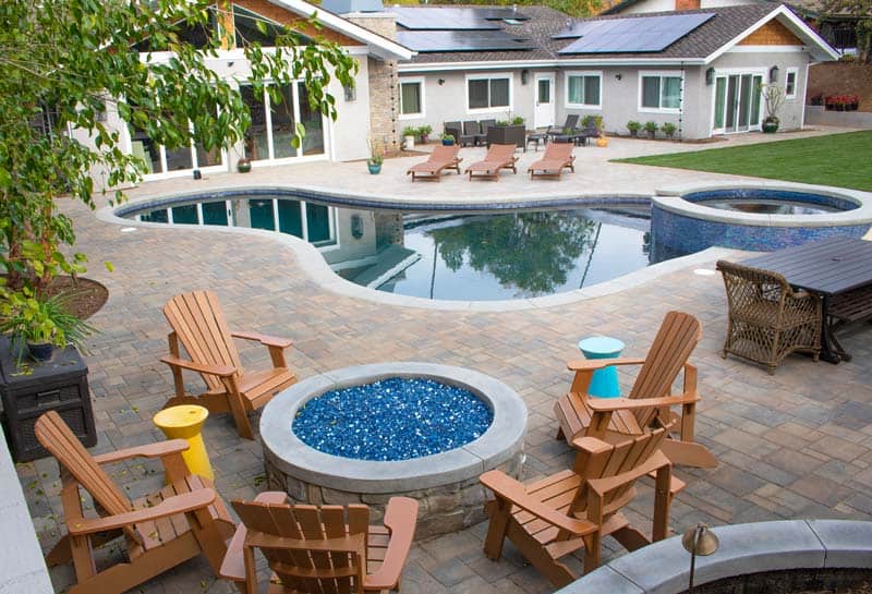 Custom backyard pool and spa surrounded by a paver patio and fire pit seating