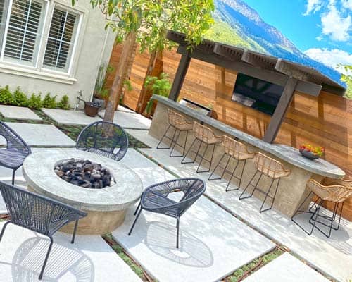 A backyard with a fire pit, bbq island and chairs.