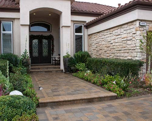 Front entry walkway with paver steps, stone veneer facade, and landscaped planting beds