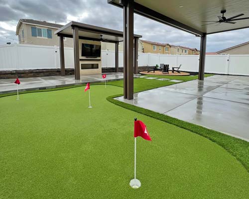 Backyard artificial putting green installed next to covered patio and concrete hardscape