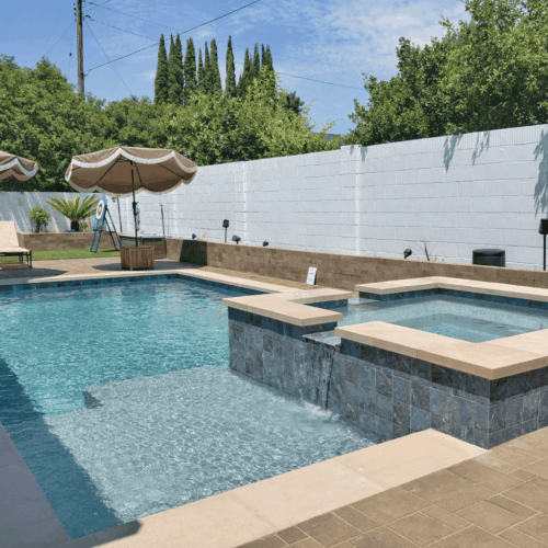 Backyard swimming pool with raised spa, waterfall feature, tanning ledge, and poolside lounge area.